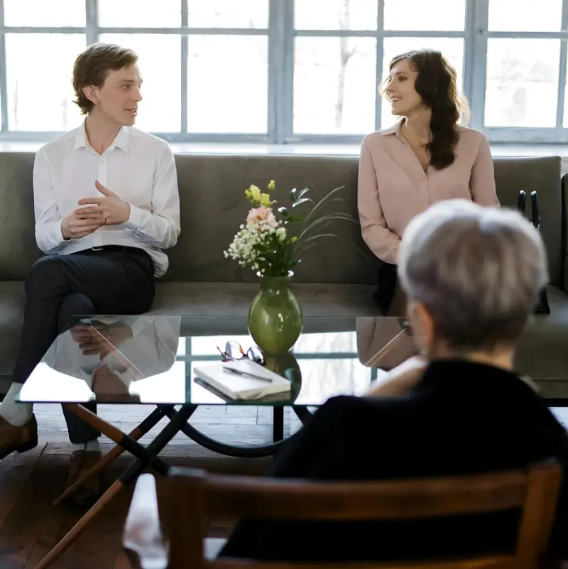 Two people sitting on a couch in front of an older woman.