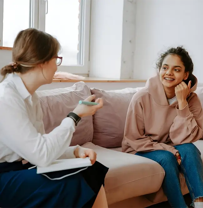 A woman sitting on the couch talking to another person.